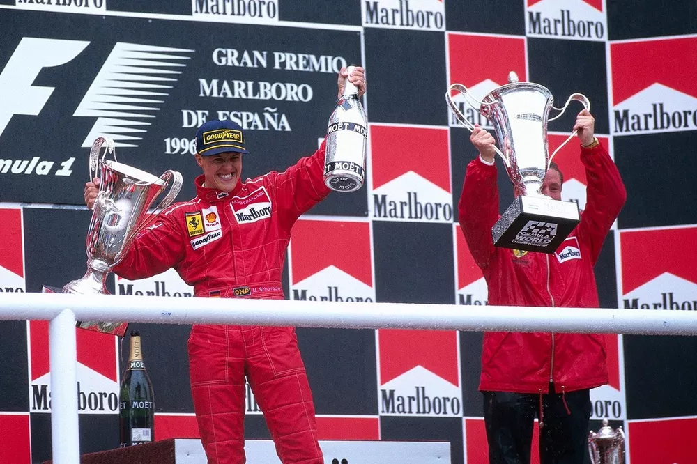 Michael Schumacher celebrates his first victory for Ferrari on the podium with team boss Jean Todt