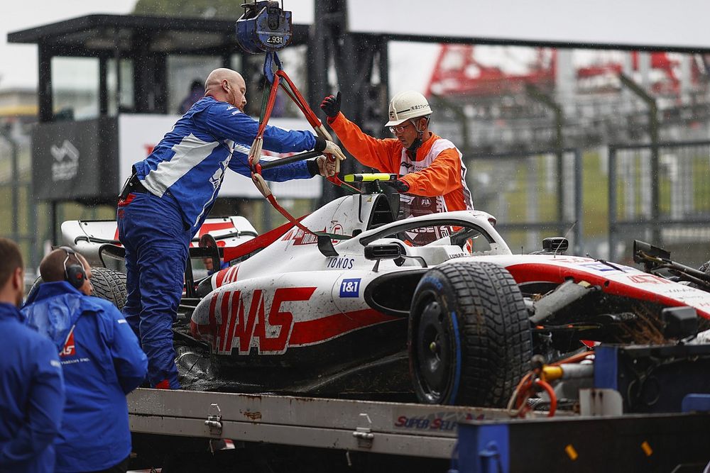 Mechanics and marshals unload the damaged car of Mick Schumacher, Haas VF-22, from a flat bed truck after FP1