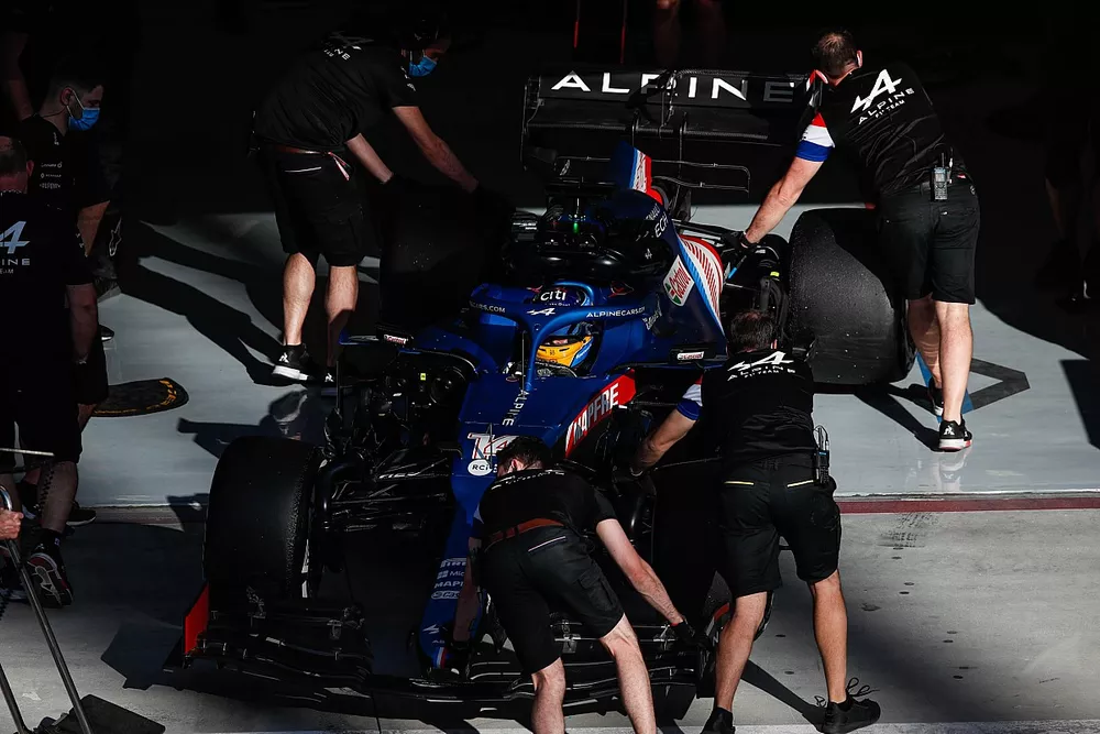 Des mécaniciens poussent la monoplace de Fernando Alonso, Alpine A521, dans son garage