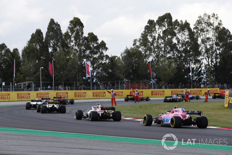 Marshals wave drivers, including Esteban Ocon, Force India VJM11 and Esteban Ocon, Force India VJM11, around debris from an opening lap accident