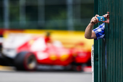 A fan leans through some bars to take a photo as Sebastian Vettel, Ferrari SF70H, passes by in the background