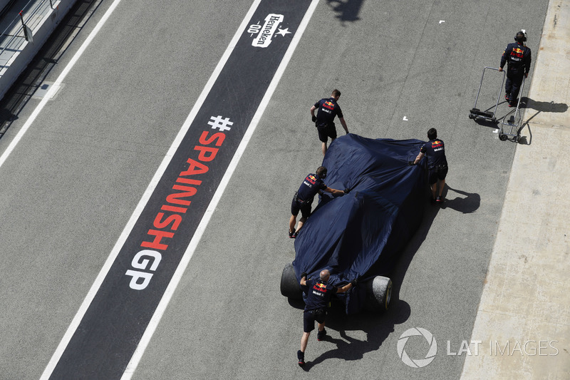 Mechanics push the damaged Daniel Ricciardo Red Bull Racing RB14 under covers in the pit lane