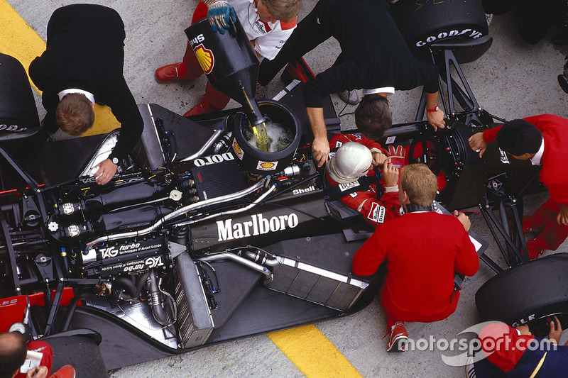 Alain Prost se sienta en su McLaren MP4/3 TAG Porsche mientras los mecánicos trabajar en el coche y recargar combustible