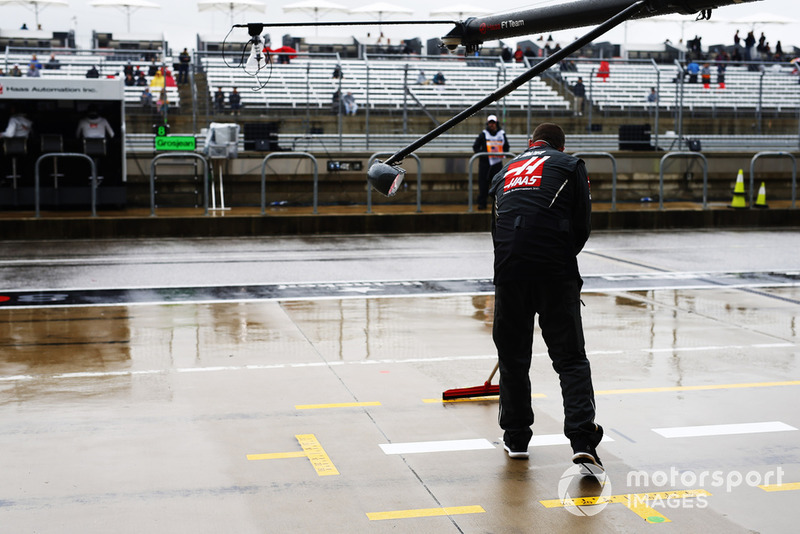 Un meccanico Haas F1 asciuga la piazzola box con una scopa